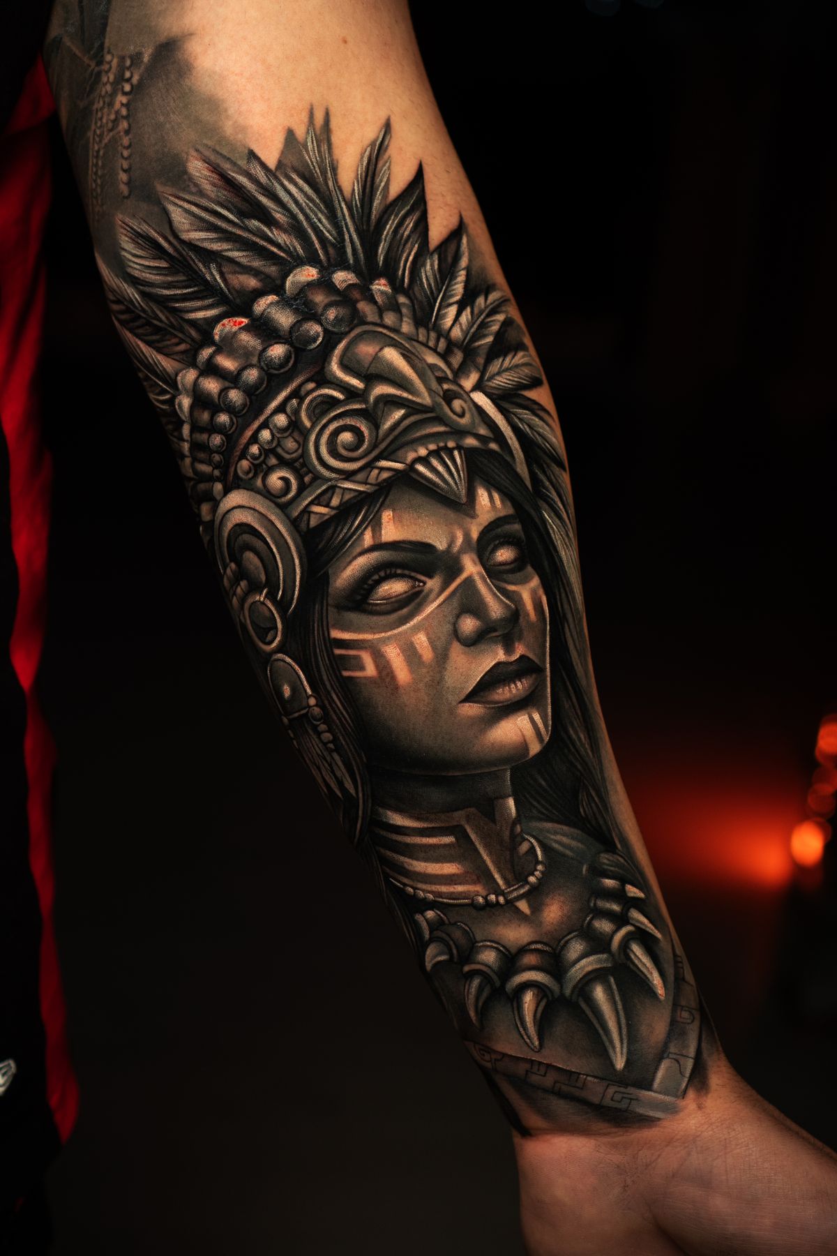 Tatuaje en antebrazo de guerrera azteca con tocado de plumas, estilo realismo Black and Grey
